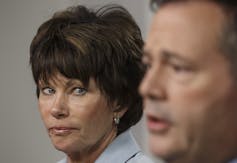 A woman with a short dark haircut looks at a man as he speaks.