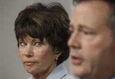 A woman with a short dark haircut looks at a man as he speaks.