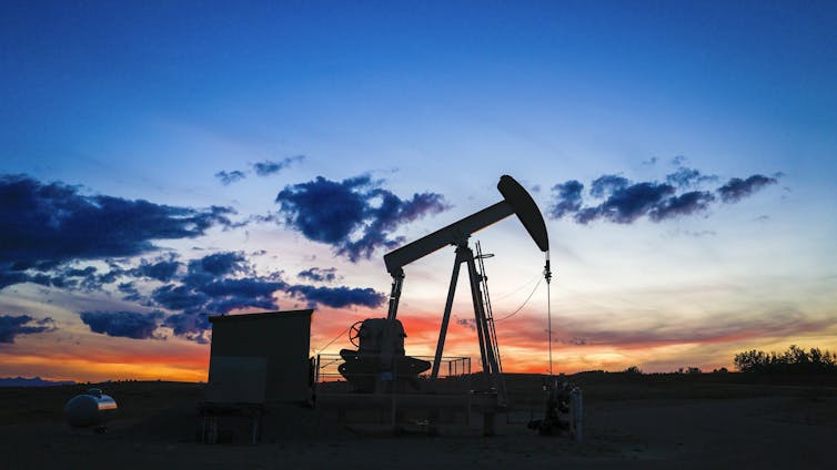 A pumpjack draws out oil from a well head as the sun sets behind it.
