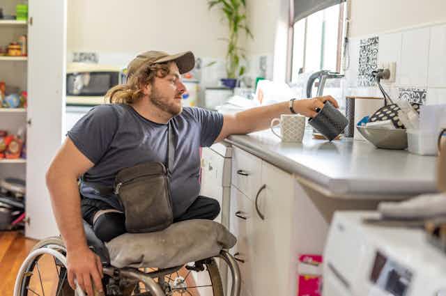 man in wheelchair reaches for coffee cup in kitchen