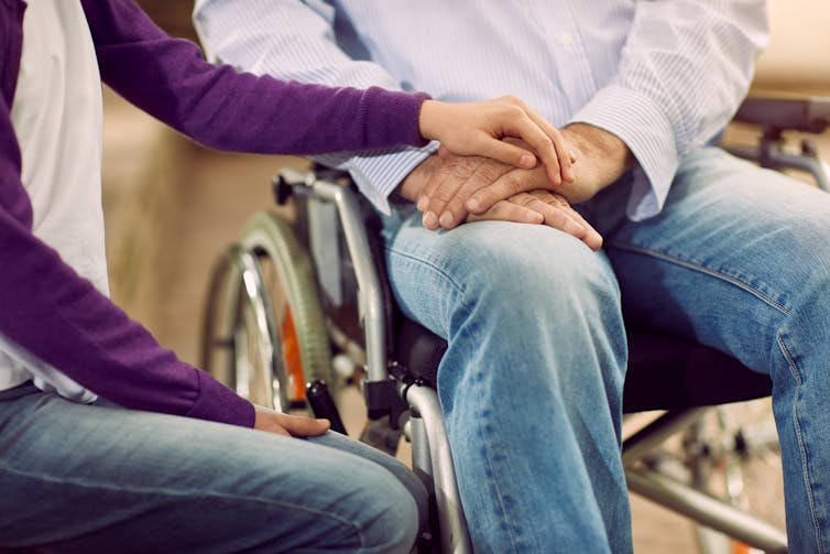 person sitting next to person in wheelchair holds their hand for comfort
