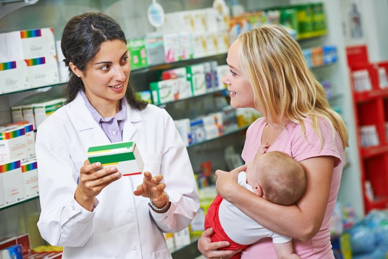 Pharmacist explains a medicine to a mother holding a young child