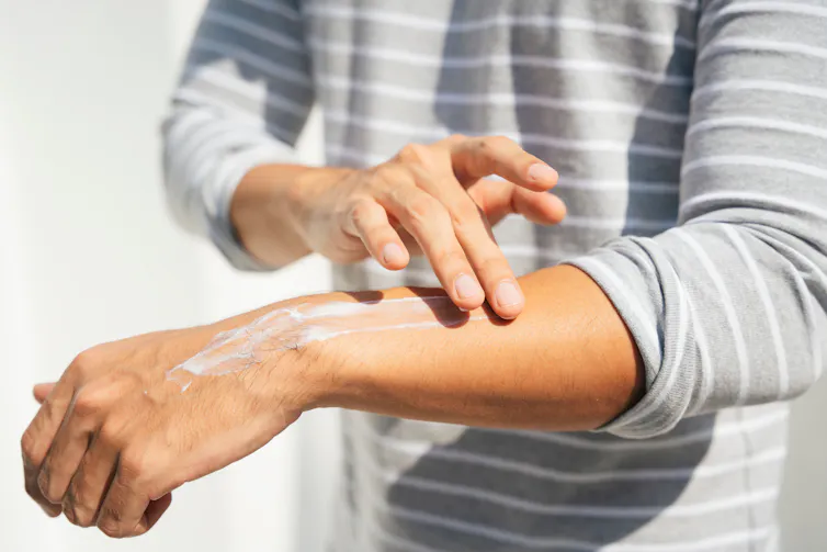 someone in a striped grey long-sleeved t-shirt applying sunscreen onto their forearm