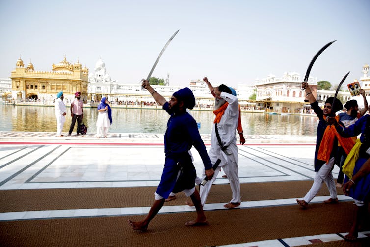 Picture of a group of men walking inside a Sikh temple carrying swords