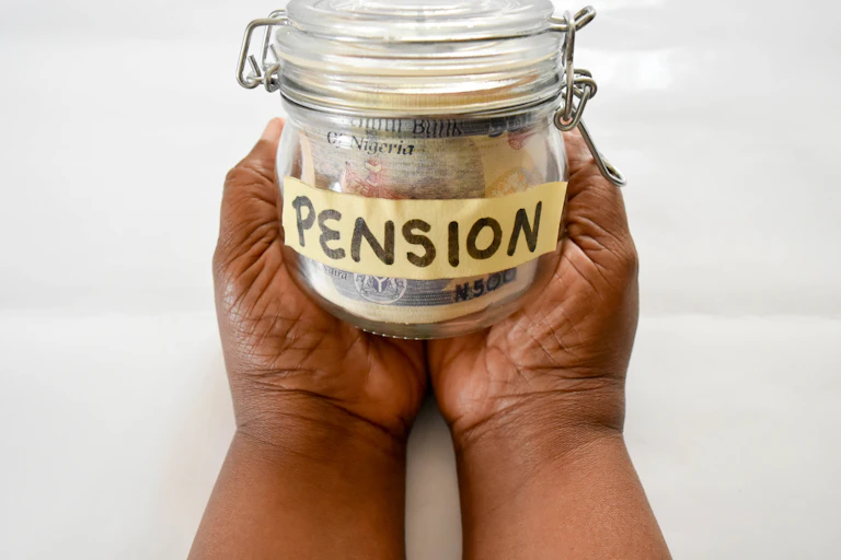 A photograph of a pair of hands holding Nigerian banknotes in a small bottle.