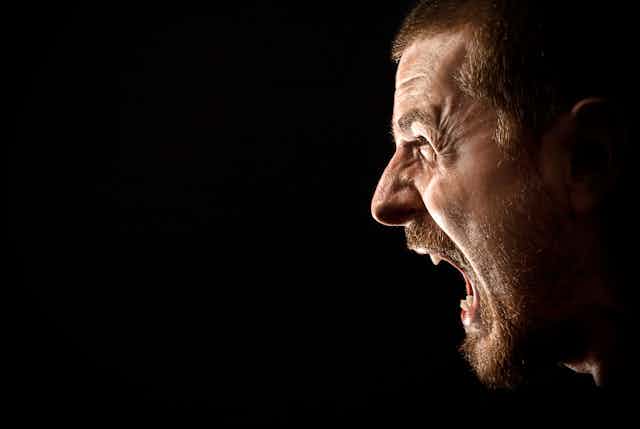 a man's face shown in profile with mouth wide open in a scream against a black background