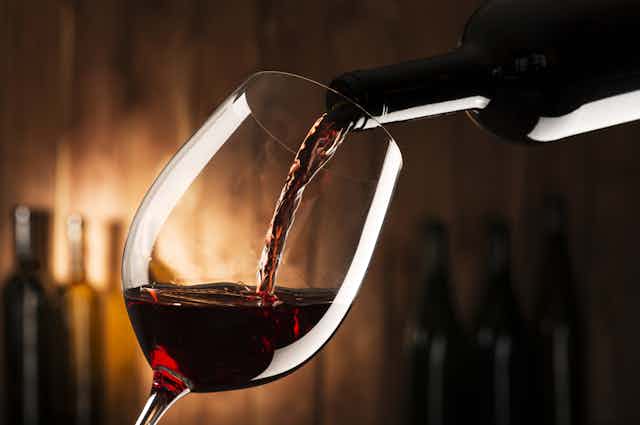 Du vin rouge passe d'une bouteille à un verre à pied