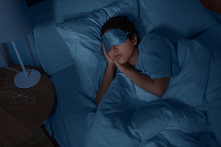 a person asleep in bed wearing a blue satin sleeping mask