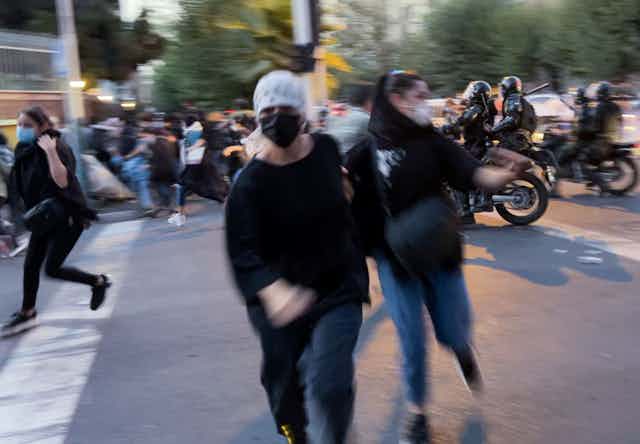 People run across a street as police on motorcycles drive through a crowd.