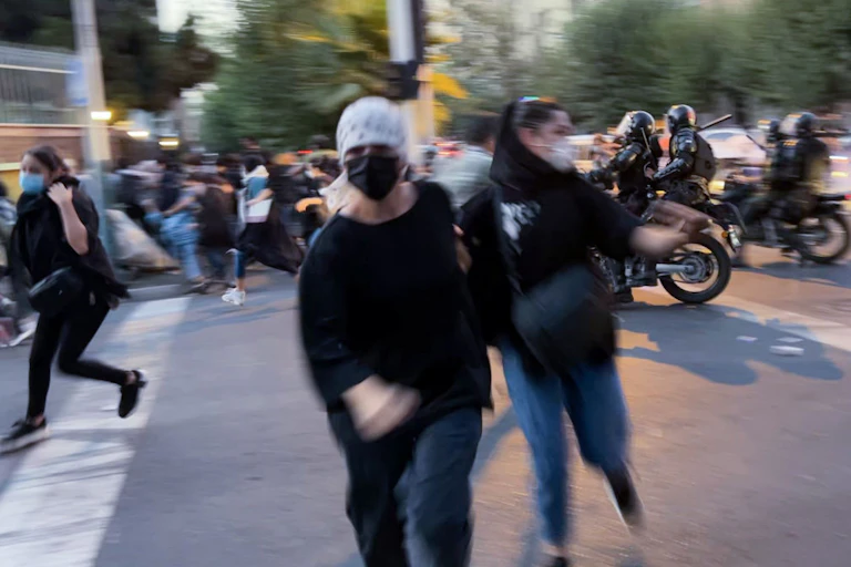 People run across a street as police on motorcycles drive through a crowd.
