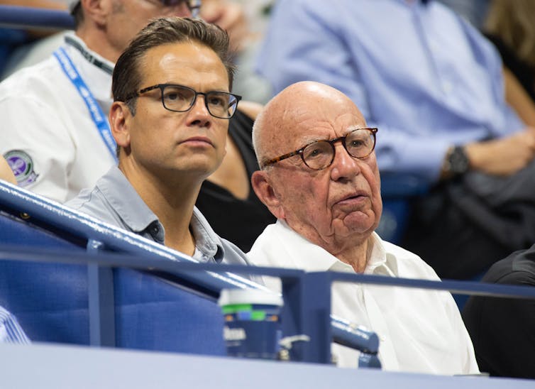 Two men in polo shirts watching some sort of sports competition.