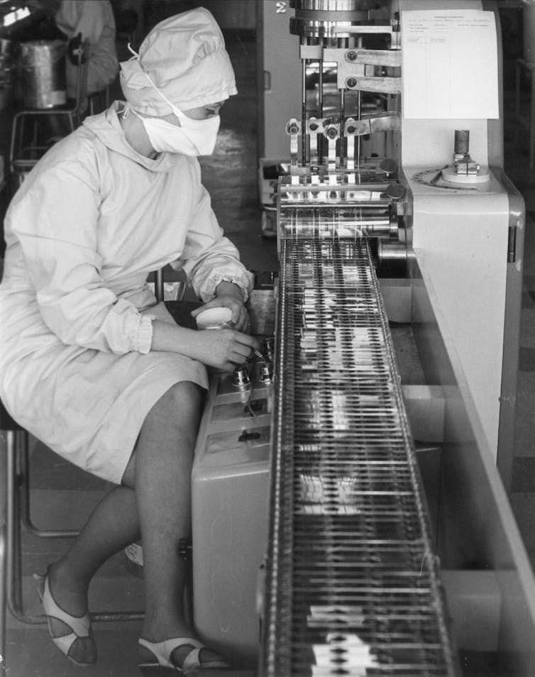 Worker monitoring penicillin capsules coming down production line