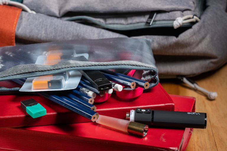 A school bag sits next to a pencil case with a vape spilling out of it.