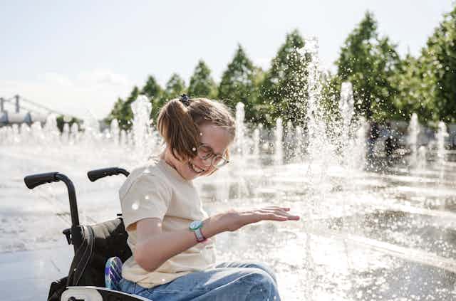 girl in wheelchair amid water fountain feature in park