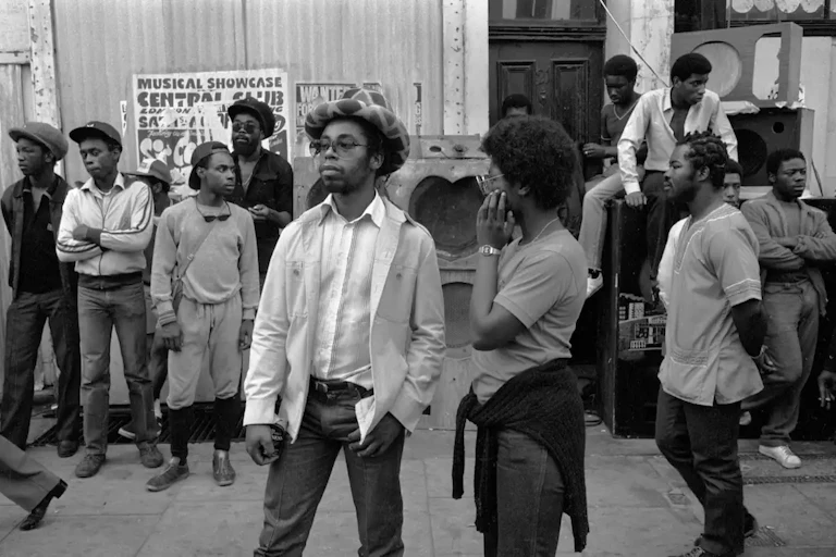 Teenagers stand around a sound system with heart shaped speakers in a black and white photograph.