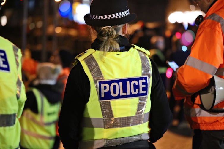 View from behind of a female Met police officer at night, in a high vis vest that reads POLICE