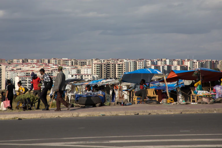 Several high-rise apartments are seen in the background as people walk past street sellers on a busy pavement.