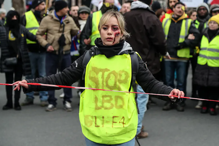 Une manifestante « gilets jaunes » grimée proteste contre les violences de certains policiers qui ont blessé plusieurs militants. Février 209