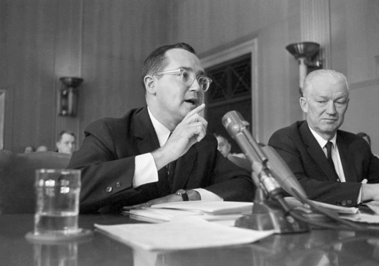 Man gestures while speaking into microphone.