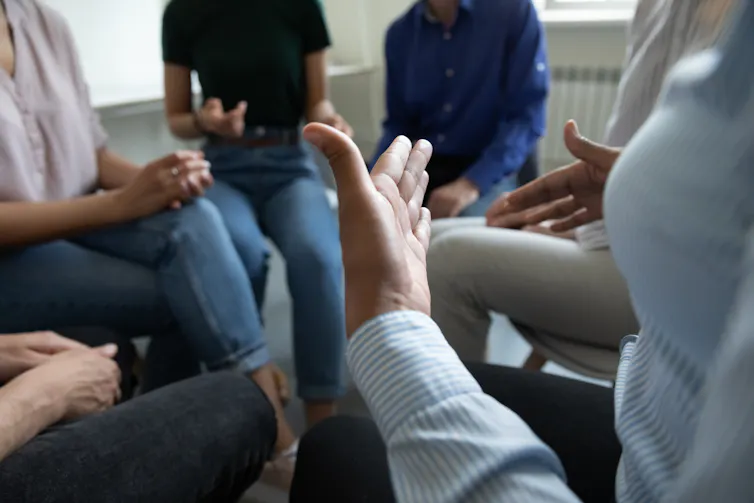 People in smart casual clothing in a circle, shoulders down, hands gesturing.