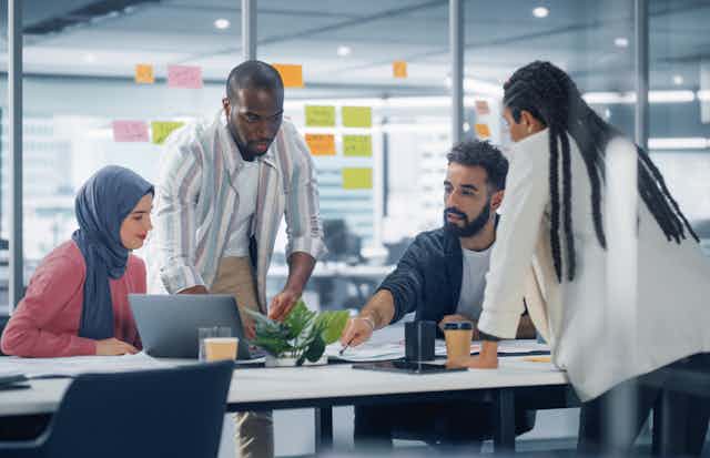 A group of people sitting and standing around a conference table, having a discussion.