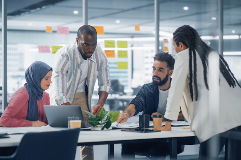A group of people sitting and standing around a conference table, having a discussion.