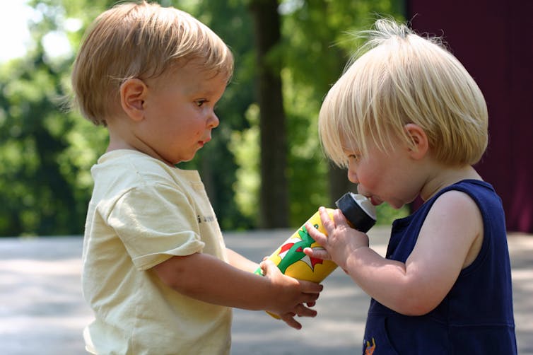 Two children seen sharing a water bottle.