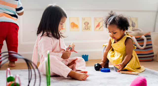 Two children seen sitting on a rug playing with toys.
