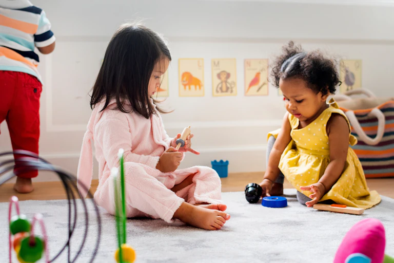 Two children seen sitting on a rug playing with toys.