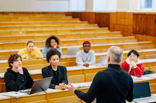 A teacher speaks to a small group of students in a lecture hall.