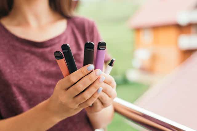 Woman holds different coloured vape pens