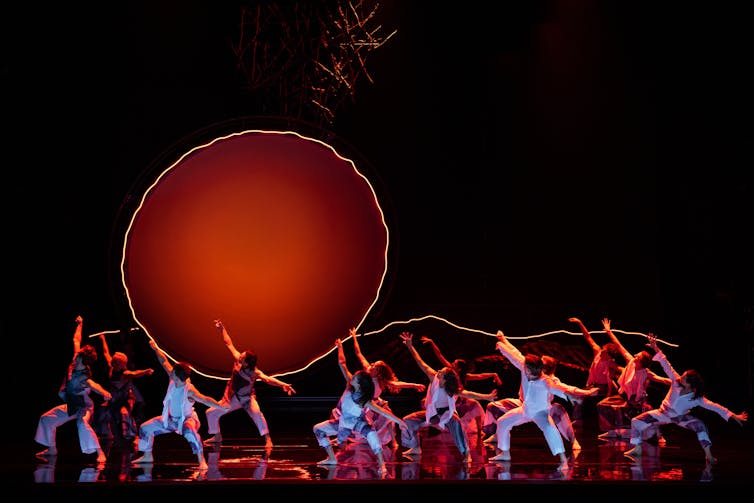 Dancers on stage under a neon orange sun.