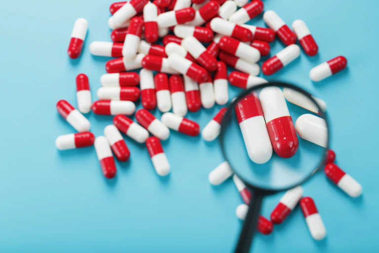 a handful of red and white pill capsules are examined with a magnifying glass on a blue background