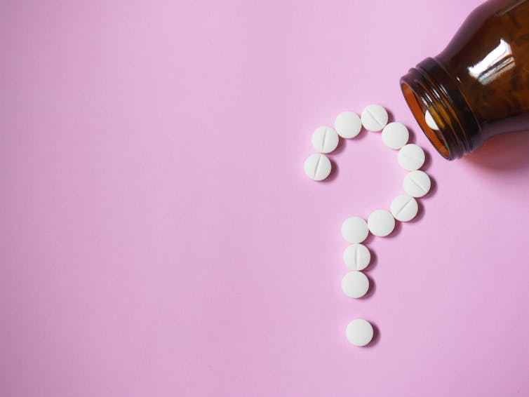 White pills spilling out of a bottle forming the shape of a question mark against a pink background
