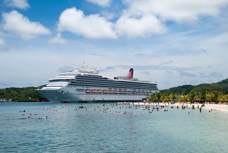 A beach full of tourists from the cruise ship moored nearby.