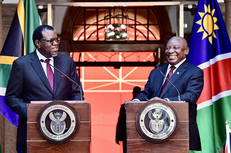 Two men in suits and ties smile at the podium, in front of the Namibian and South African flags.
