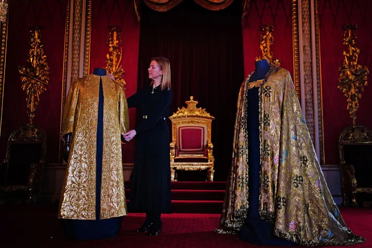 A lady in black stands besides a display of royal garments.