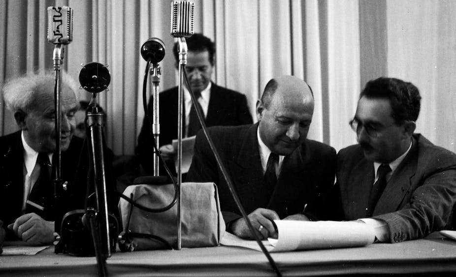  Israel declares independence. Left to right David Ben Gurion, Moshe Kaplan and Moshe Sharett sign the declaration in front of microphones.