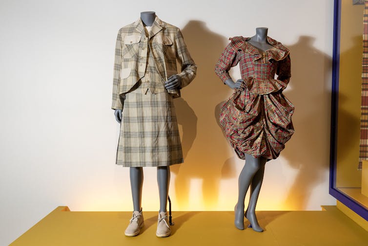 A skirt suit and draped tartan dress hanging on mannequins.