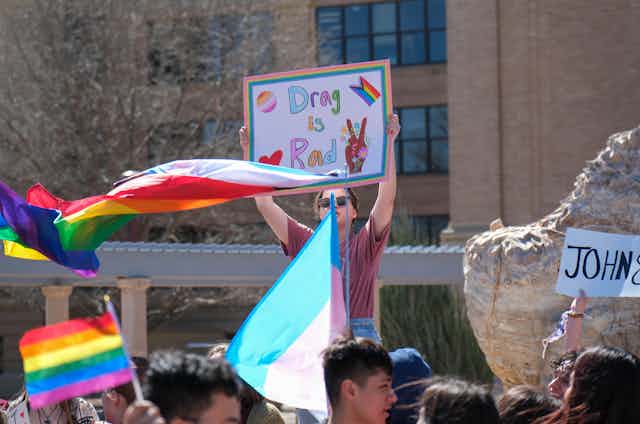 People at a protest waving rainbow flags, a woman carried a placard that reads: drag is rad.