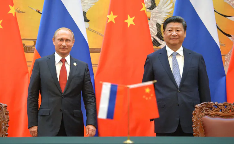 Two men, presidents Xi and Putin, stand in front of flags.