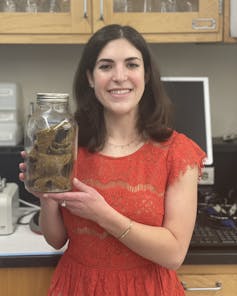 smiling woman holds a liter-size jar with scrunched up knitting in it