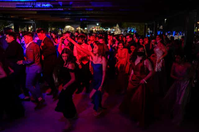 a crowd of young people dance in a dark room with red light