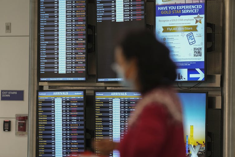 A woman walks in front of a screen displaying flight schedules.