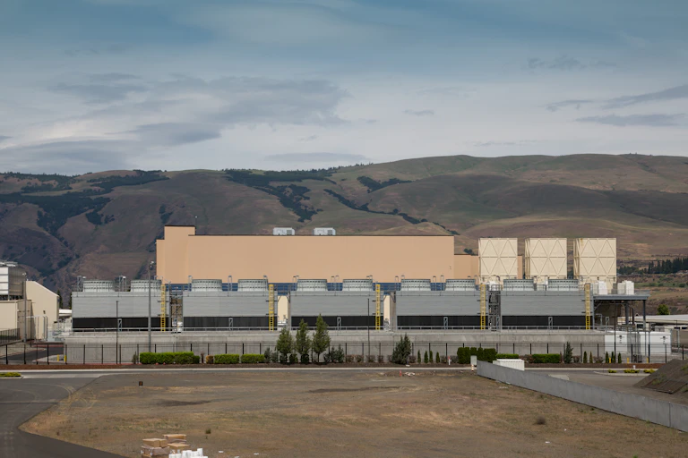 a large industrial building with hills in the background