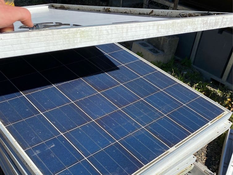 hand lifts up one of a pile of old solar panels