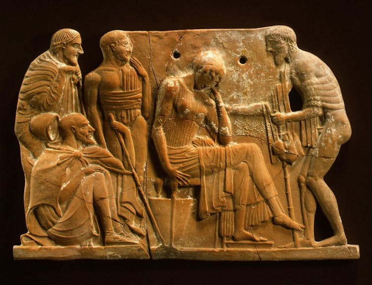 Une plaque sculptée représente une femme assise, la tête dans les mains, entourée d’hommes