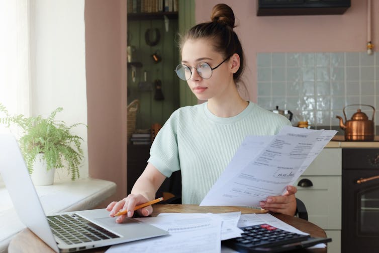 A young woman works with a calculator and laptop with sheets of paper.
