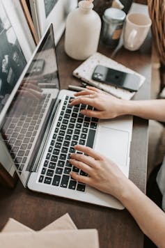 A young person works on a computer next to a cup, book and phone.
