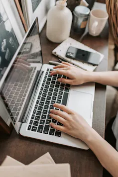 A young person works on a computer next to a cup, book and phone.